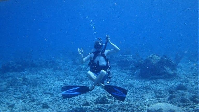 A diver kneeling on the sand, working through a skill