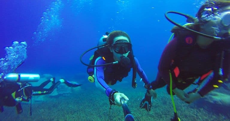 Two divers swimming side by side through open blue