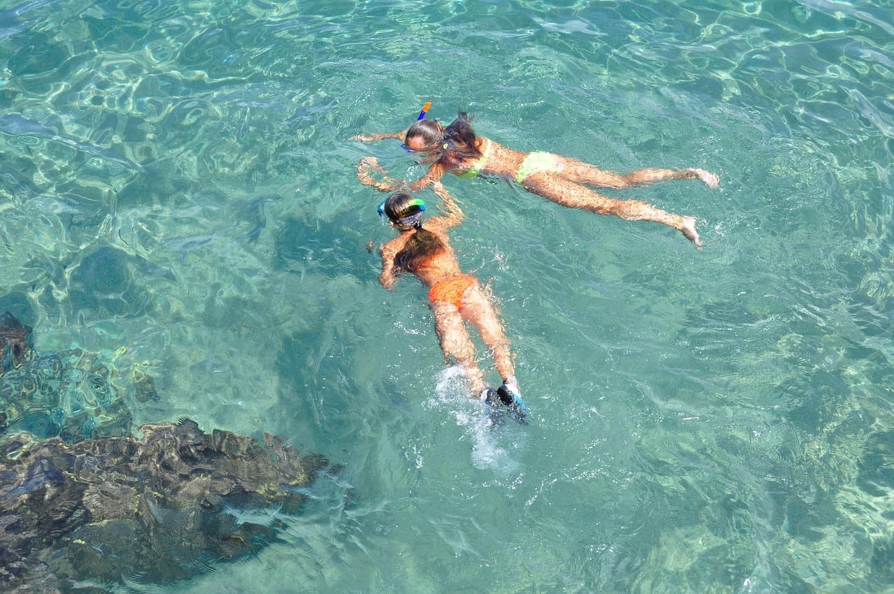 Two snorkellers gliding over a shallow reef in clear turquoise water
