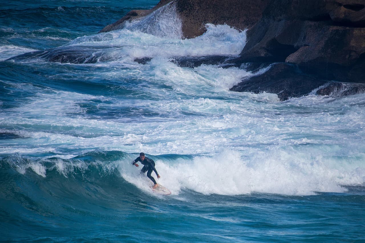 A surfer riding the face of a breaking wave below a rocky headland